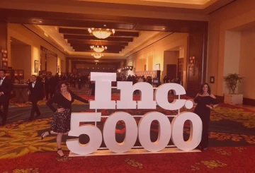 Two Women On Either Side Of Inc. 5000 Logo Statue At Business Event