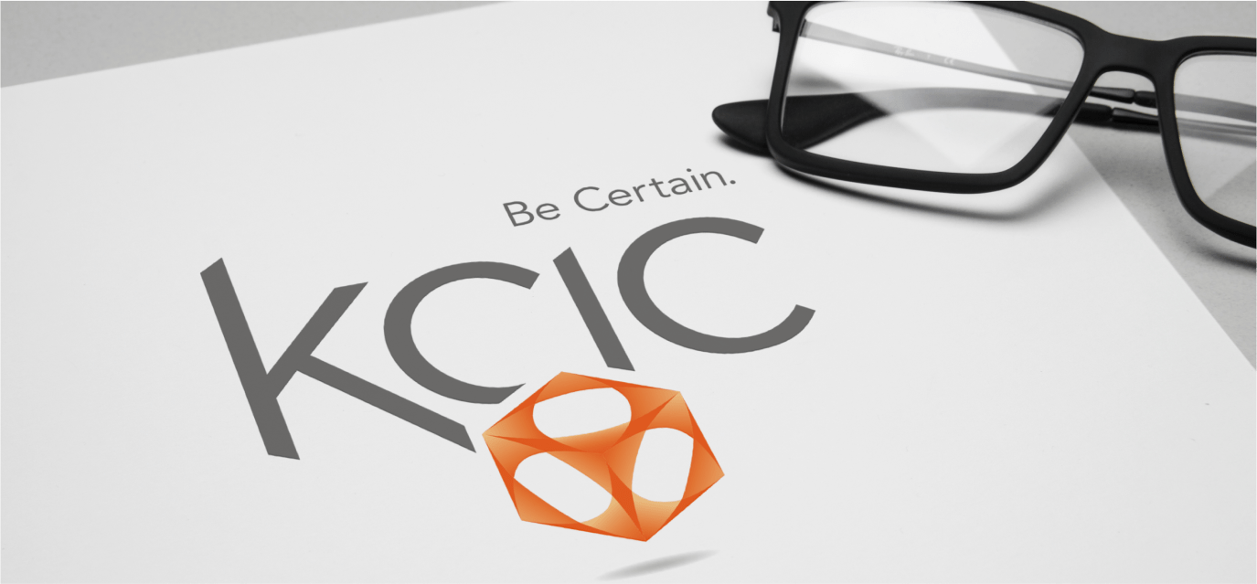 Piece of paper that says "Be Certain: KCIC" with an orange logo, and a pair of glasses on top of the paper