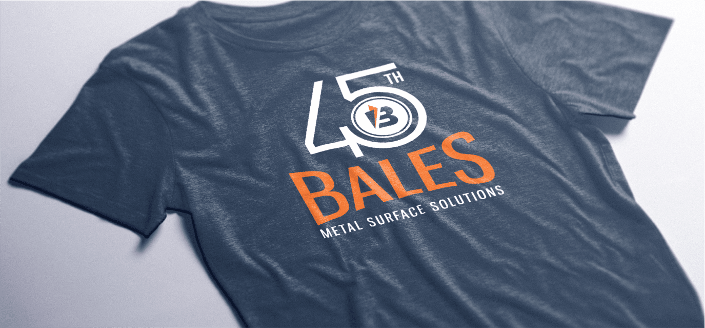 A navy blue t-shirt with an orange Bales Metal Surface Solutions company logo