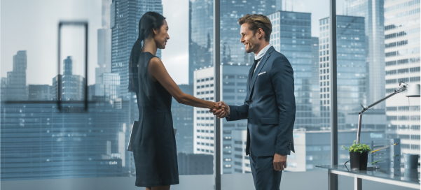 A man and a woman in an executive office suite, smiling and shaking hands